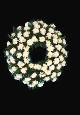 O coroană funerară circulară din flori albe și frunze verzi, aranjate îngrijit