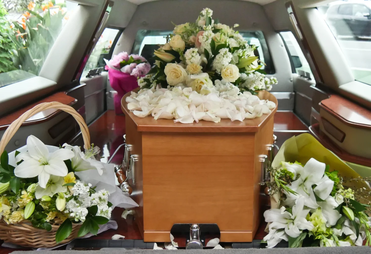 Un sicriu de lemn împodobit cu petale de trandafiri albi și un aranjament floral