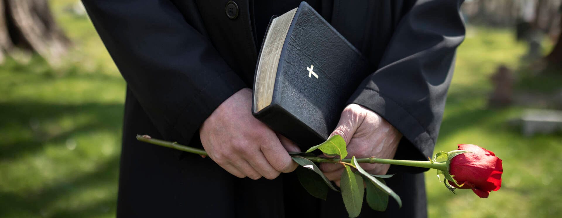 Barbat tinand flori si o Biblie in cimitir, moment de reculegere